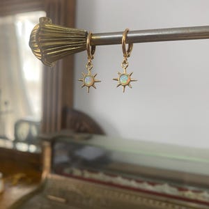 May include: Gold hoop earrings with a dangling star charm featuring a white opal stone.