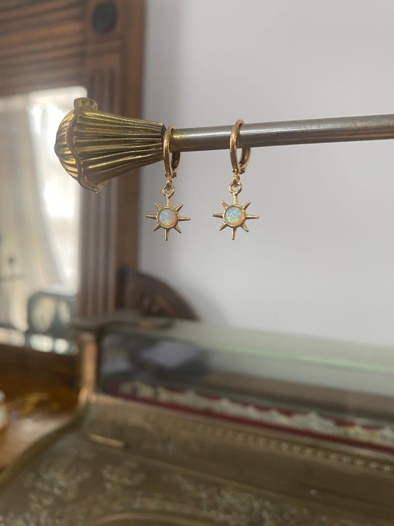 May include: Gold hoop earrings with a dangling star charm featuring a white opal stone.