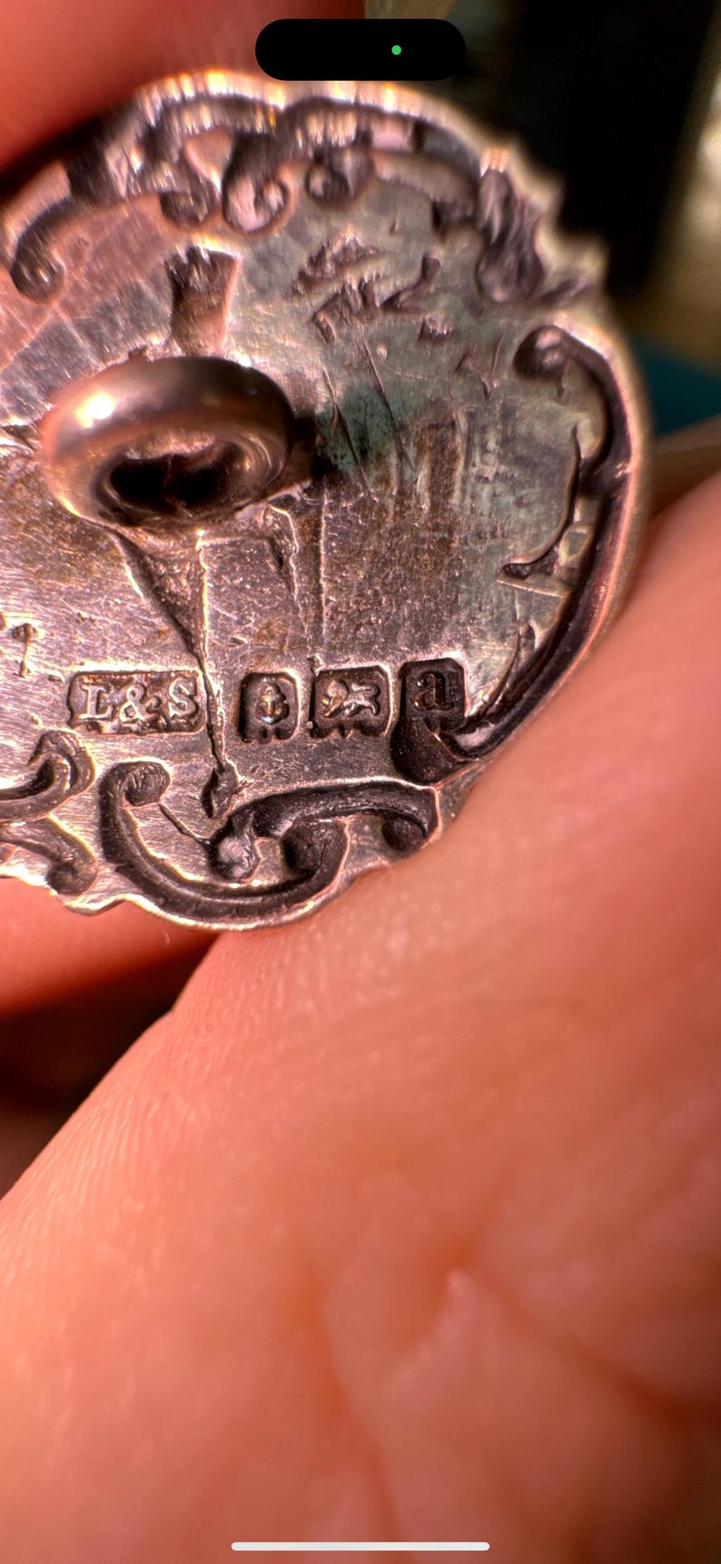 May include: Close-up of a silver button with intricate floral designs. The back of the button has the markings "L&S" and a crown.