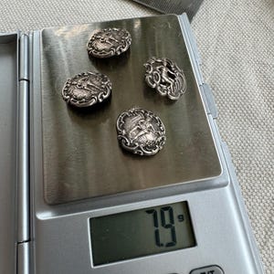 May include: Four silver buttons with intricate designs, weighing 7.9 grams, on a digital scale.