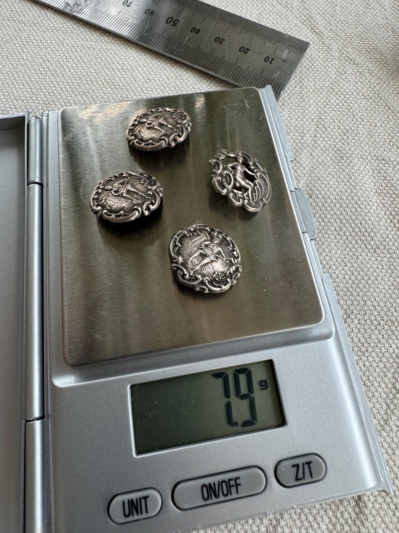 May include: Four silver buttons with intricate designs, weighing 7.9 grams, on a digital scale.