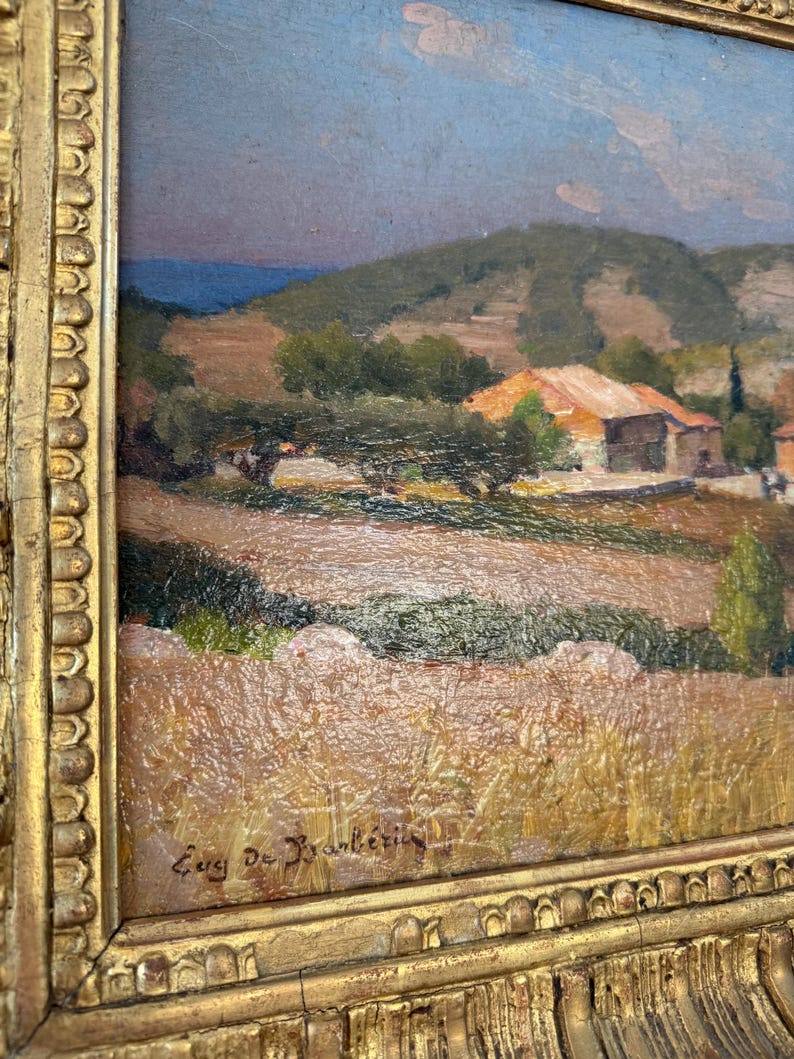 Puede incluir: Una pintura de un paisaje con un pueblo en la distancia. El cielo es de un azul claro con algunas nubes. Las colinas son verdes y marrones. El pueblo est&aacute; formado por peque&ntilde;as casas con techos rojos. La pintura est&aacute; firmada "Eug De Brant&eacute;tis" en la esquina inferior derecha.