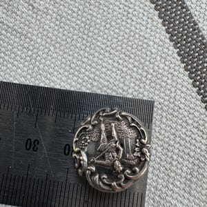 May include: Silver-toned button with an intricate design featuring a golfer swinging a club. The button is oval-shaped and has a detailed floral border.