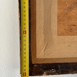 Puede incluir: Primer plano del borde inferior de un marco de imagen de madera con un respaldo de papel marr&oacute;n. Una cinta m&eacute;trica amarilla es visible a lo largo del borde izquierdo del marco, con los n&uacute;meros del 20 al 43 visibles.