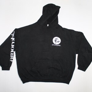 May include: Black hooded sweatshirt with a front pocket and white text on the left sleeve and chest. The sleeve text reads "amorphis" vertically. The chest features a circular design with the word "amorphis" below it.