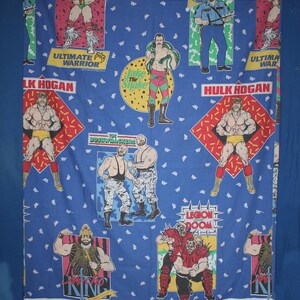 May include: Blue fabric with vibrant illustrations of wrestlers. The design includes images of Hulk Hogan, The Ultimate Warrior, and others, with text labels such as "Hulk Hogan" and "Ultimate Warrior."
