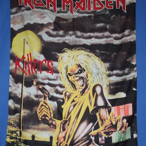 May include: A black Iron Maiden "Killers" banner featuring the band's mascot, Eddie, holding a bloody axe. The banner has a dark, ominous background with a full moon and the band's logo in red.