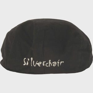 Könnte beinhalten: Schwarze Flatcap mit dem Wort "Silverchair" in weißer Schrift auf der Rückseite gestickt. Die Kappe ist aus einem dunklen Stoff gefertigt und hat eine runde Form.