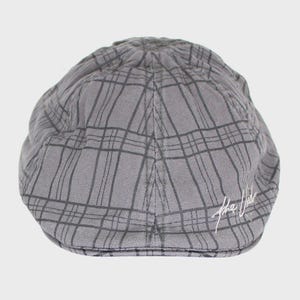 May include: A gray newsboy cap with a plaid pattern. The cap has a rounded crown and a short, stiff brim. The cap has the text "the vibe" in white script on the side.