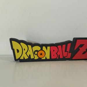 May include: A black, yellow, and red Dragon Ball Z logo. The logo features the words "DRAGON BALL" in yellow, a star in an orange circle, and the letter "Z" in red. The logo is on a white surface.