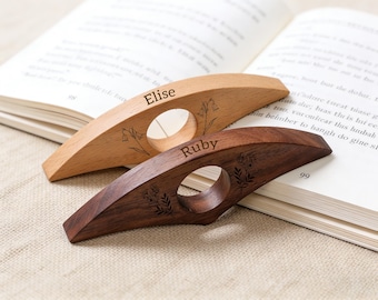 May include: Two wooden book page holders, one light-colored and one dark, with floral engravings. The light-colored holder has the name "Elise" engraved, while the dark one has "Ruby". Both have a circular opening for the finger.