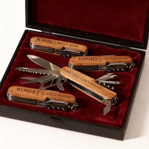May include: A set of personalized wooden pocket knives in a black box with a red velvet interior. Each knife is engraved with a name and role, such as "Best Man" or "Groomsman". The knives have multiple tools.