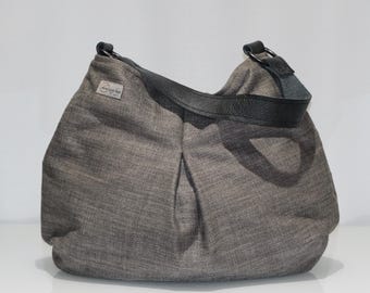 May include: A gray fabric shoulder bag with a black leather strap. The bag has a rounded shape and a small label on the side. The strap is attached to the bag with metal rings.