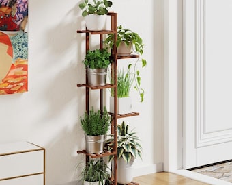 May include: A tall, dark brown wooden plant stand with multiple shelves, holding various potted plants. The plants include green leafy varieties in white and silver containers. The stand is positioned against a white wall, with a door and artwork visible.