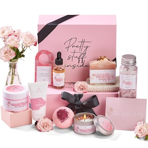 May include: A pink gift box with a black ribbon and the text "Pretty stuff inside". The box contains a variety of bath and body products, including a rose-scented soap, bath salts, body butter, a bath bomb, and a candle. The box also includes a small rose bouquet and a card that says "From Within to You".