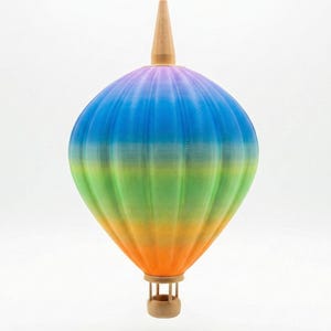Könnte beinhalten: Hängeleuchte in Form eines Heißluftballons mit Regenbogenfarben. Der Ballon hat einen Holzaufsatz und einen kleinen Korb am Boden. Die Lampe wird von einem dünnen weißen Kabel gehalten.