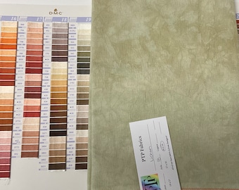 May include: A piece of light green fabric with a mottled texture next to a D.M.C. color chart. A white tag labeled PTP Fabrics Lichen is attached to the fabric, which features a visible grid pattern and an orange stitched edge at the bottom.