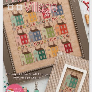 May include: A cross-stitch pattern titled Prim Village featuring rows of colorful houses in teal, yellow, pink, red, blue, and green on tan fabric. The pattern includes small and large charts, a metal house charm, and a smaller framed sample.