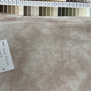 May include: A piece of light brown, mottled fabric with a serged edge. A white tag is attached, reading: Name: Small Potatoes, Aida: 14 16 18 20, Linen: 28 32 36 40 46 56, www.lapinloops.com. A color reference chart with numbered thread swatches is visible.