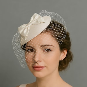 Puede incluir: Sombrero tipo pillbox de color marfil con un lazo de satén y un delicado velo de red. El sombrero es de diseño clásico, adecuado para bodas o eventos formales. El velo es de malla fina. El sombrero mide unos 15 cm de diámetro.