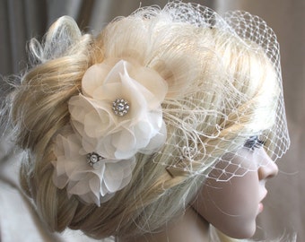 May include: A white bridal veil with a delicate floral hairpiece featuring two white chiffon flowers with a rhinestone center. The veil is made of a fine mesh material and is perfect for a wedding or special occasion.