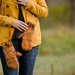 May include: A pair of crocheted mittens in shades of orange, brown, and yellow, with a button detail. The mittens are hanging from a yellow jacket.