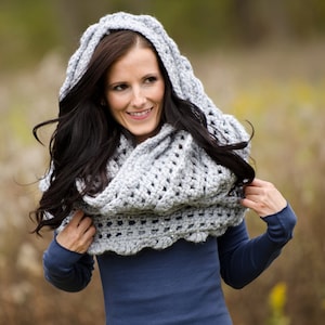 May include: A gray crocheted cowl with a hood. The cowl is worn by a person with long dark hair. The cowl is made with a lacy stitch pattern.