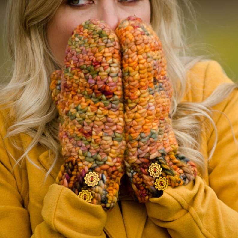 May include: A pair of colorful crocheted mittens with yellow flower embellishments. The mittens are made with a variety of shades of brown, orange, and red yarn.