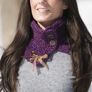 Puede incluir: Una bufanda de cuello de tortuga de punto morado con botones decorativos y un adorno floral.