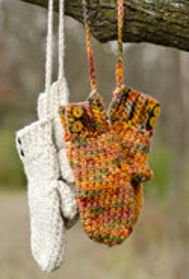 May include: Two pairs of crocheted mittens hanging on a tree branch. One pair is beige and the other is a multi-colored mix of orange, yellow, and brown.