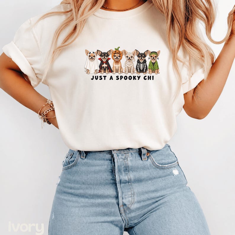May include: An ivory short-sleeve t-shirt featuring a graphic of six Chihuahua dogs dressed in various Halloween costumes, including a ghost, vampire, pumpkin, mummy, skeleton, and monster, with the text "JUST A SPOOKY CHI" printed below.
