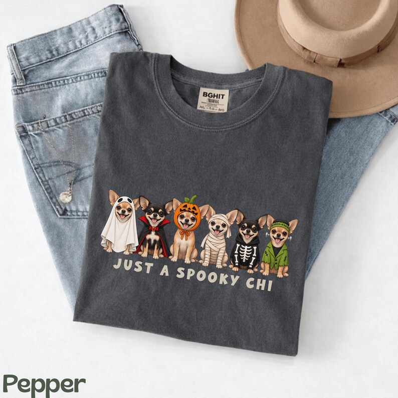 May include: A charcoal gray t-shirt featuring a graphic of six Chihuahua dogs in various Halloween costumes, including a ghost, vampire, pumpkin, mummy, skeleton, and Frankenstein's monster, with the text "JUST A SPOOKY CHI" printed below.