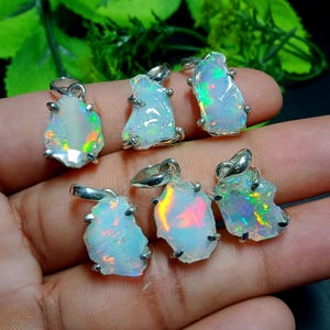 May include: A collection of six opal pendants with silver-colored bails. The opals are rough-cut, displaying iridescent flashes of color. Each pendant is unique in shape and size, showcasing natural variations. The opals are set with small silver prongs.