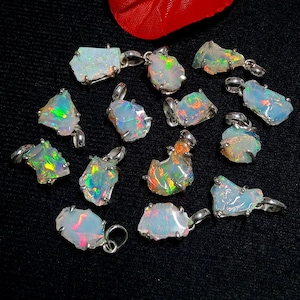 Op de afbeelding: Een verzameling opalen hangers met zilverkleurige ophangogen. De opalen vertonen een scala aan kleuren, waaronder iriserende flitsen van groen, oranje en blauw. De hangers zijn geplaatst tegen een zwarte achtergrond.
