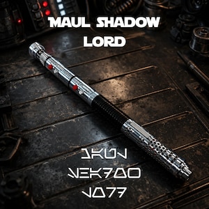 May include: A silver and black lightsaber with the text "MAUL SHADOW LORD" and "AKUN NEK700 N077". The lightsaber has red buttons and a textured black grip. The lightsaber is on a dark, metallic surface.