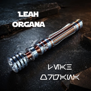 May include: A lightsaber with a silver, copper, and red design. The hilt has a ribbed texture and a clear emitter. The text "LEAH ORGANA" and "LUKE SKYWALKER" are displayed in white.