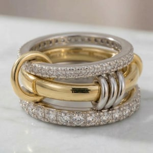 May include: A multi-band ring featuring a combination of gold and silver tones. The ring has three bands, with the top and bottom bands encrusted with small, clear stones. The middle band is gold, and the bands are interlocked.