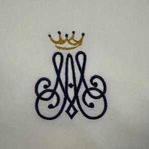 May include: Embroidered monogram featuring a gold crown above a navy blue letter 'A' with ornate swirls, on a white backdrop. Suitable for a towel or textile item.