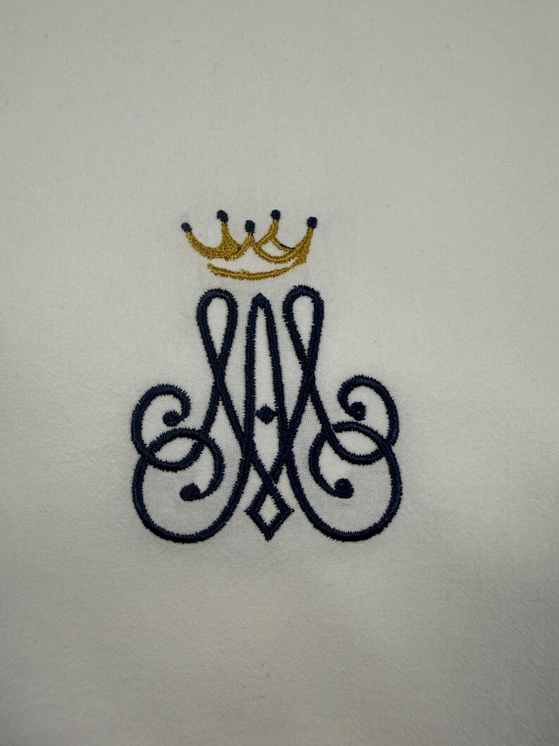 May include: Embroidered monogram featuring a gold crown above a navy blue letter 'A' with ornate swirls, on a white backdrop. Suitable for a towel or textile item.