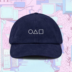 Könnte beinhalten: Eine marineblaue Baseballkappe aus Cord mit einem weißen gestickten Design aus einem Kreis, einem Dreieck und einem Quadrat.