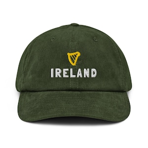 May include: A dark green corduroy baseball cap with the word "IRELAND" embroidered in white, and a gold harp emblem. The cap has a curved brim and a structured crown, suitable for casual wear.