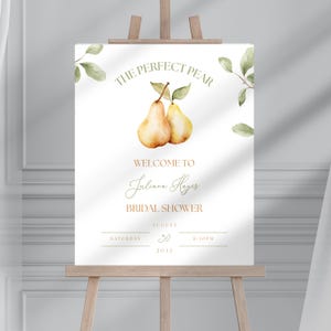 May include: A white sign on a wooden easel with the text "THE PERFECT PEAR" and "WELCOME TO Juliana Hayes BRIDAL SHOWER". The sign features watercolor illustrations of pears and leaves, with the date August 30, 2032.