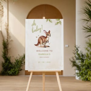 May include: A baby shower welcome sign on a wooden easel. The sign features a watercolour illustration of a kangaroo with its joey, the words "Oh baby!" and "Welcome to Isabella's Baby Shower" in elegant script, and the date.