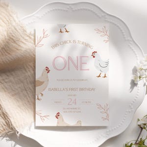 Op de afbeelding: Een lichtroze en witte verjaardagsuitnodiging met de tekst "THIS CHICK IS TURNING ONE". De uitnodiging bevat illustraties van kippen en bloemaccenten. De tekst "ISABELLA'S FIRST BIRTHAY" is ook opgenomen, samen met de datum en tijd.