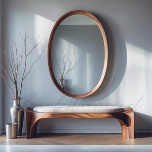 May include: A wooden bench with a white cushion, a large oval mirror with a wooden frame, and a silver vase with dried branches in front of a light grey wall.