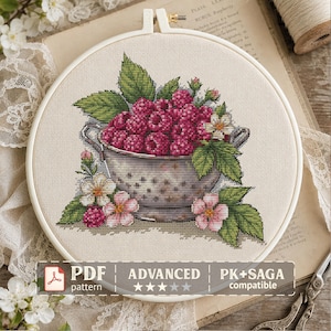 May include: A cross-stitch embroidery project in a circular wooden hoop featuring a metal colander filled with deep red raspberries, green leaves, and small white and pink flowers. The text PDF pattern ADVANCED PK+SAGA compatible is visible.