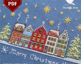 May include: A cross-stitch design featuring a row of colorful houses with lit windows, snowflakes, and Christmas trees on a blue background. The text "Merry Christmas" is stitched below the houses. The design is labeled "Intermediate".