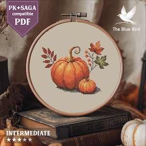 May include: A cross-stitch embroidery hoop featuring a fall pumpkin design. The design includes a large orange pumpkin, a smaller pumpkin, and autumn leaves. The text "The Blue Bird" and "PK+SAGA compatible PDF" are visible.