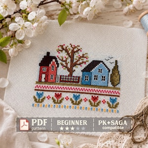 May include: A cross-stitch pattern on white Aida fabric featuring a red house, a blue house, a central tree, and a row of colorful tulips. The text reads PDF pattern, beginner, and PK+SAGA compatible. The design includes small birds in the sky.