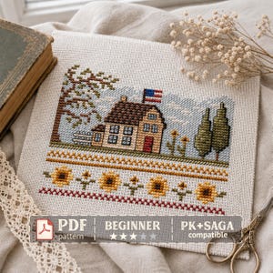 May include: A cross-stitch embroidery on light fabric featuring a house with a brown roof, a red door, and an American flag on the roof. The scene includes a tree, two evergreen trees, and a border of yellow sunflowers. Text reads PDF pattern.